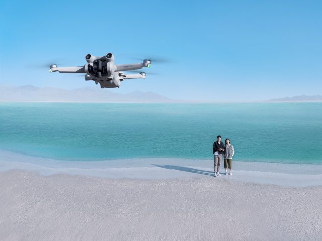 DJI Mini 3 Pro Drohne am Strand mit Pärchen im Hintergrund