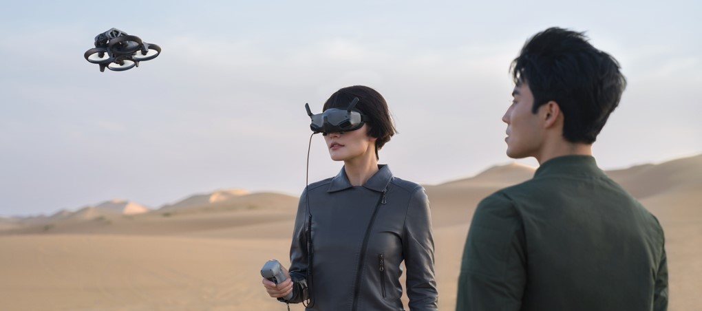 Frau im Hintergrund fliegt DJI Avata FPV Drohne mit VR-Brille