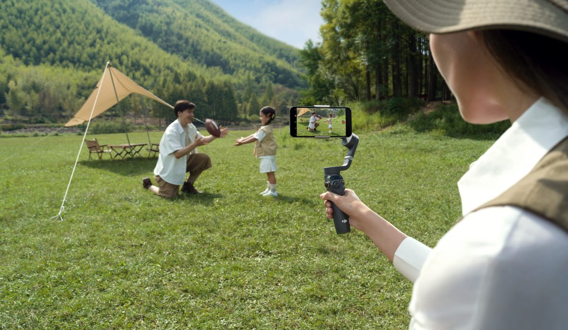 Frau filmt Mann und Kind mit Smartphone-Gimbal vor Zelt in der Natur