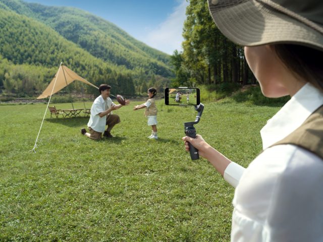 Frau filmt Mann und Kind mit Smartphone-Gimbal vor Zelt in der Natur