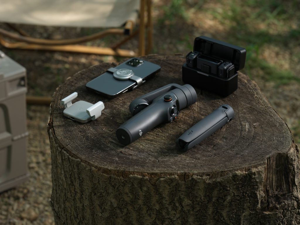 DJI Osmo Mobile mit Smarthphone und Zubehör liegt auf Baumstumpf im Wald