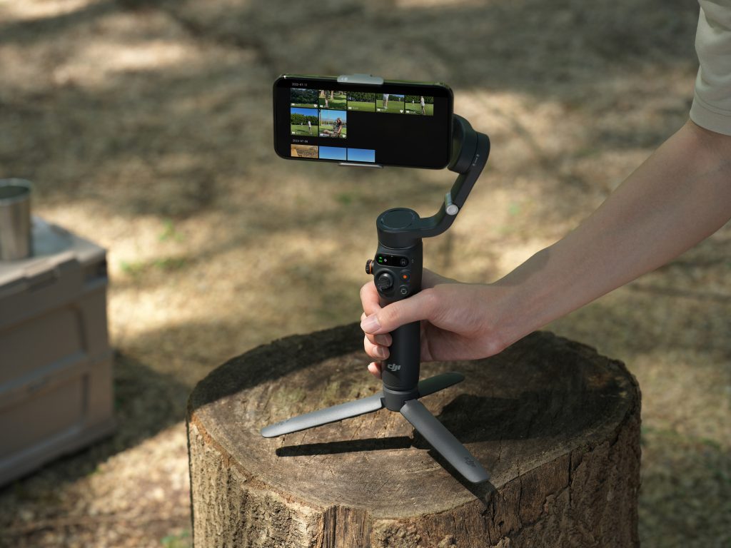 Hand stellt Smartphone-Tripod DJI OM 6 auf Baumstumpf im Wald