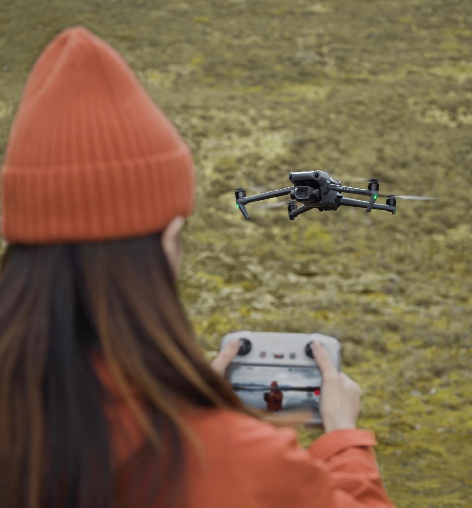 Frau mit oranger Jacke und Mütze fliegt DJI Mavic 3 Classic Drohne