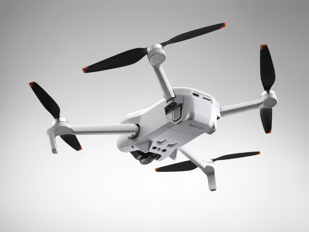 Unteransicht auf fliegende DJI Mini 3 Drohne vor hellgrauem Hintergrund