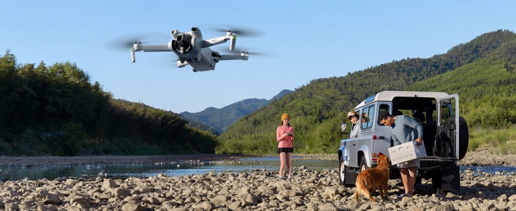 DJI Mini 3 Drohne fliegt über Flußlandschaft mit Familie an Landrover