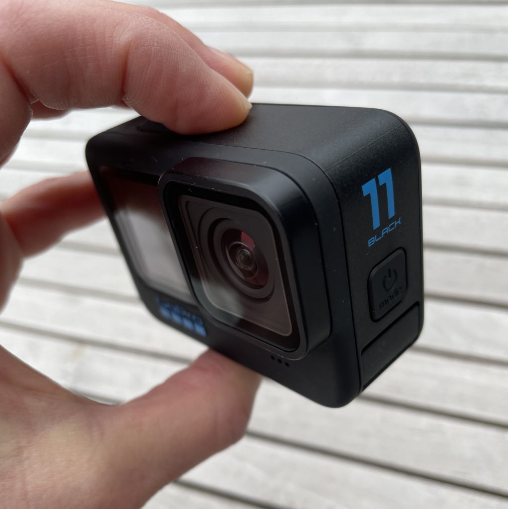 GoPro HERO11 Black in den Fingern gehalten über Holzhintergrund