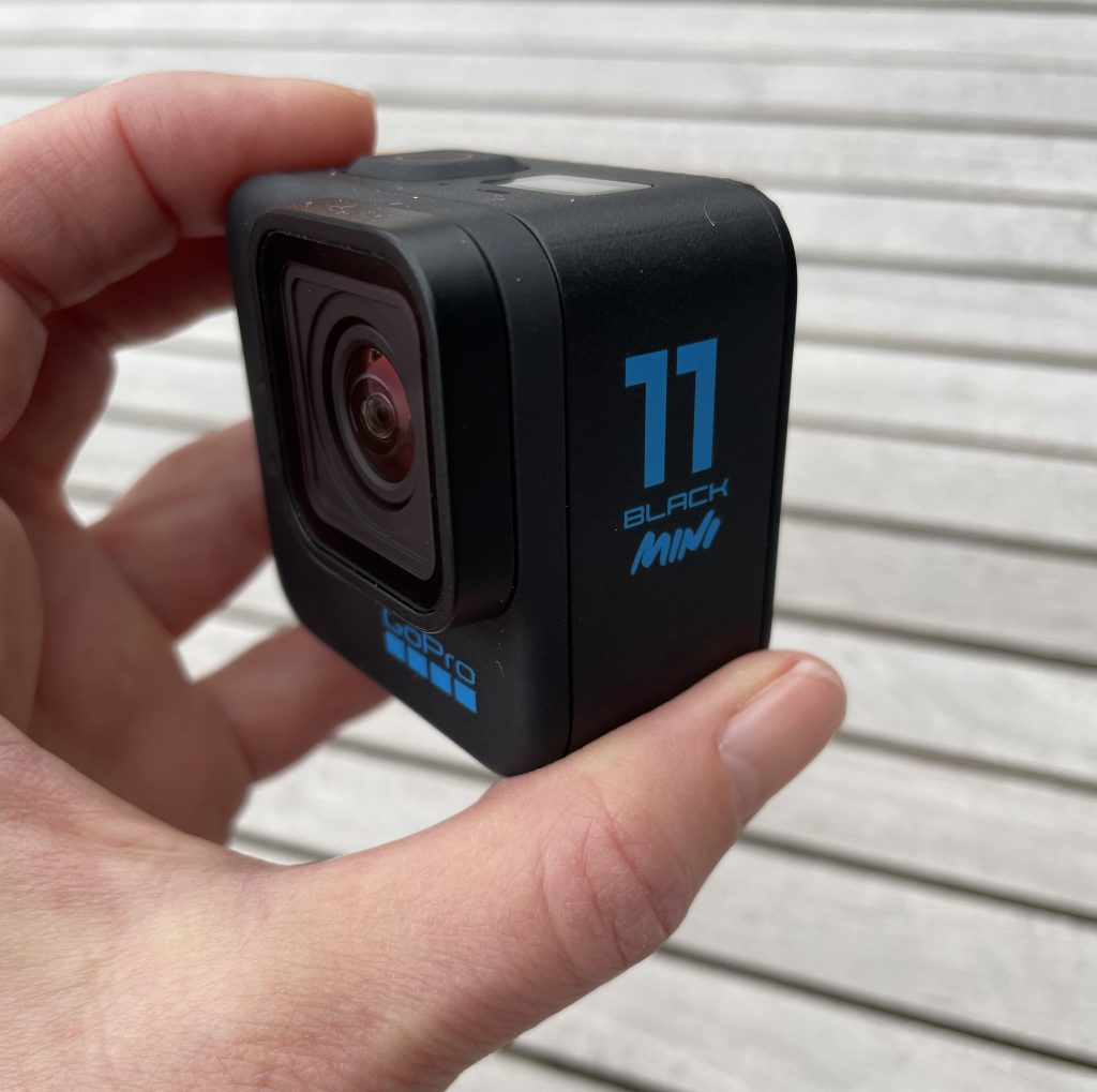 GoPro HERO11 Black Mini in den Fingern gehalten über Holzhintergrund