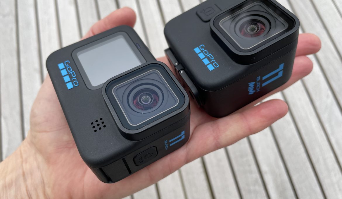 GoPro HERO11 Black und Mini auf einer Handfläche über Holzhintergrund