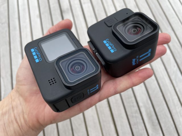 GoPro HERO11 Black und Mini auf einer Handfläche über Holzhintergrund
