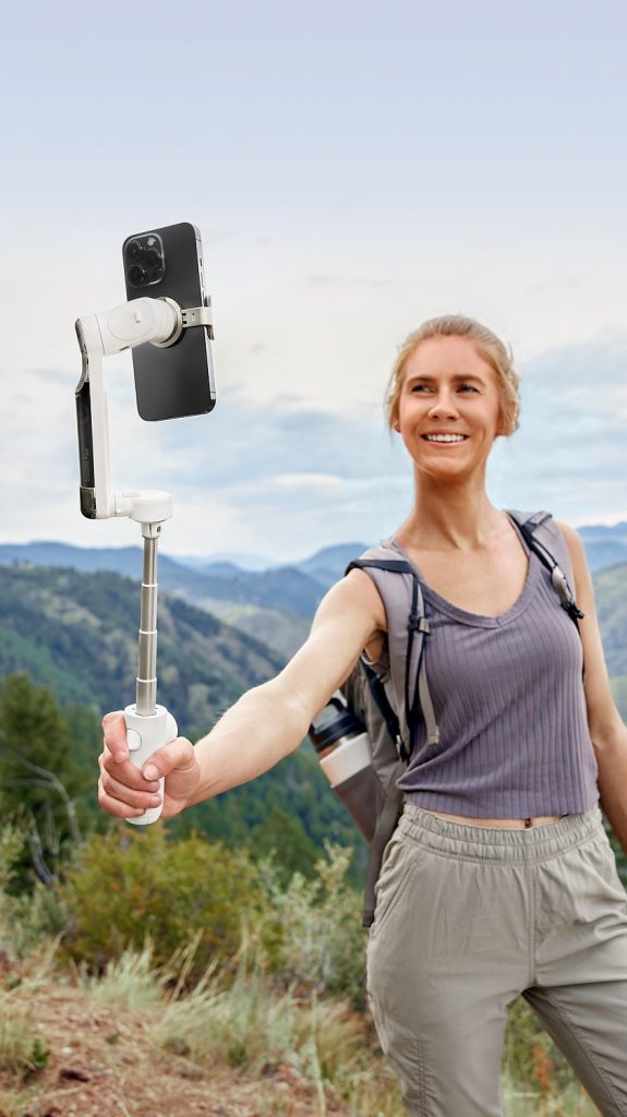 Frau hält Selfie-Gimbal vor Outdoor-Berglandschaft