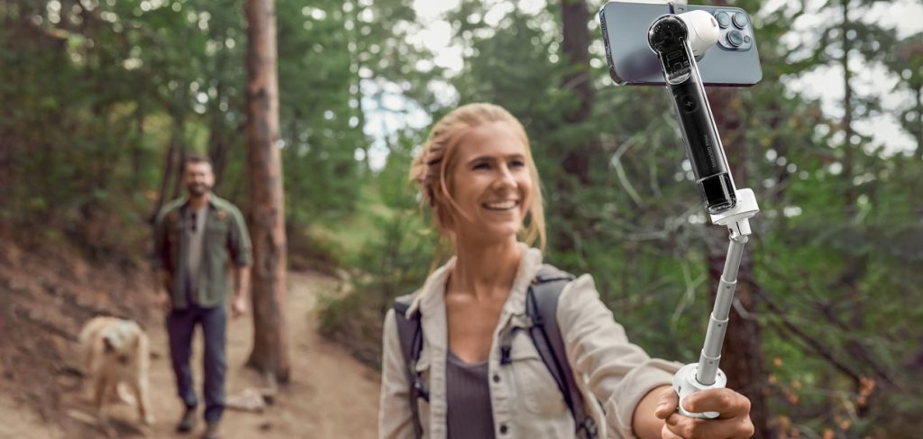 Frau hält Smartphone-Gimbal Flow von Inta360 vor Waldhintergrund