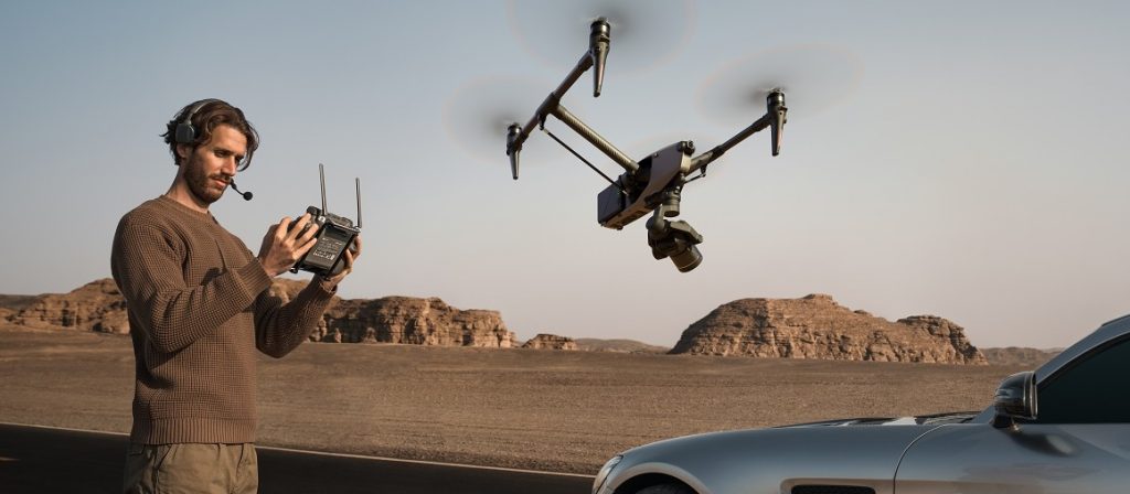 Mann mit Remote fliegt DJI Inspire 3 Drohne über Auto vor Wüstenkulisse