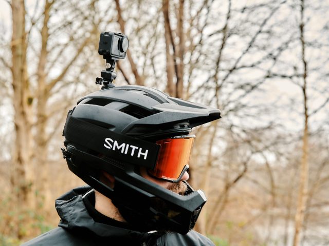 MTBer mit Vollvisier-Helm und Actioncam auf dem Helm vor Waldhintergrund