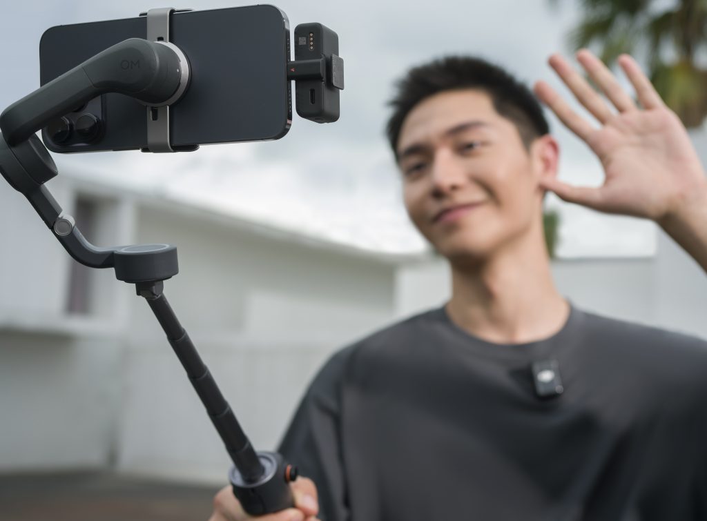 Mann winkt für Selfie in Smartphone Gimbal DJI OM6 mit neuem DJI Mic 2