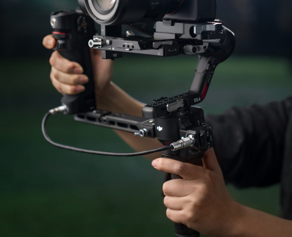 Hand hält Griff des neuen DJI Ronin 4 Gimbals mit Zubehör