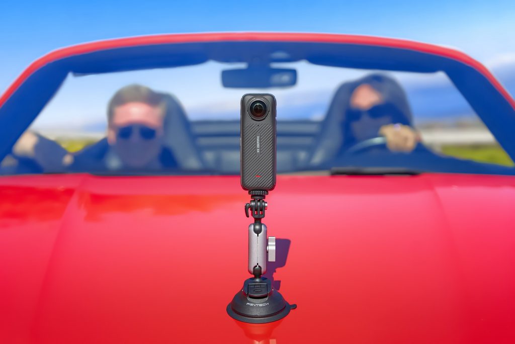 Insta360 X4 auf roter Kühlerhaube von Sportwagen mit Pärchen im Fond