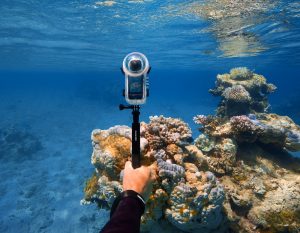 Hand hält Insta360 X4 mit Tauchgehäuse über Unterwasser-Riff