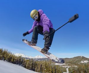 Snowboarder springt über Piste mit Insta360 X4 und Selfie-Stick in der Hand