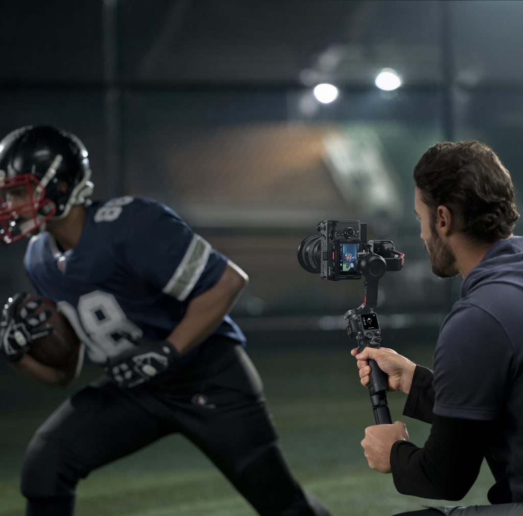 Mann filmt mit DJI RS 4 Gimbal Rugbyspieler im Lauf in Stadion mit Nachtlicht